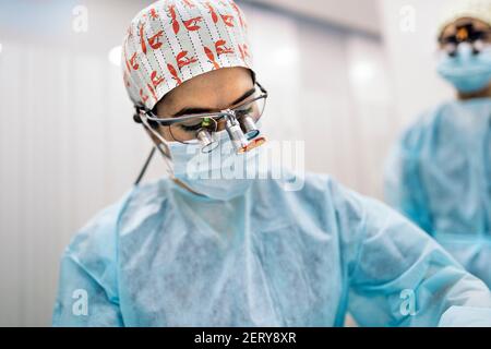 Photo de l'équipe féminine portant des masques faciaux et des loupes dentaires pendant la chirurgie. Banque D'Images