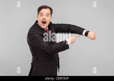 Homme qui montre un nouveau modèle, meilleure montre intelligente. Prise de vue en studio. Isolé sur fond gris. Homme d'affaires charmant avec costume noir, cravate rouge et musac Banque D'Images