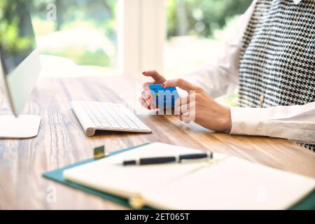 Prise de vue rognée de la main d'une femme tout en tenant sa carte de crédit et en effectuant des opérations bancaires en ligne sur un ordinateur. Banque D'Images