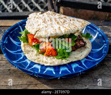 Souvlakia cuit au feu d'un camping. Servi sur une assiette bleue avec des tomates rouges, des légumes verts et du pain pita Banque D'Images