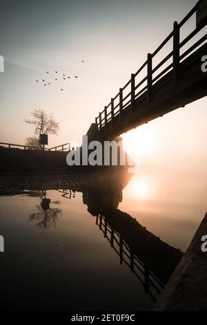 Lever de soleil depuis le pont en bois au-dessus de la rivière réfléchi dans le canal magnifique reflet orange cristal encore tranquille oiseaux d'eau voler dans le ciel Banque D'Images