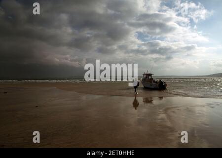 Bateau de pêche sur la plage de St Ives, Cornouailles, Angleterre, Royaume-Uni avec figure marchant vers la caméra, réflexions dans le sable humide, ciel spectaculaire de tempête approchant Banque D'Images