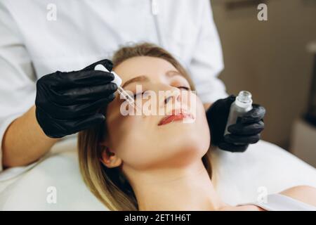 osmologiste appliquant l'essence de sérum vitamines essentielles huiles l'eau dans le visage pour améliorer la peau du client. Un spécialiste de la beauté fait des soins de beauté pour le patient Banque D'Images