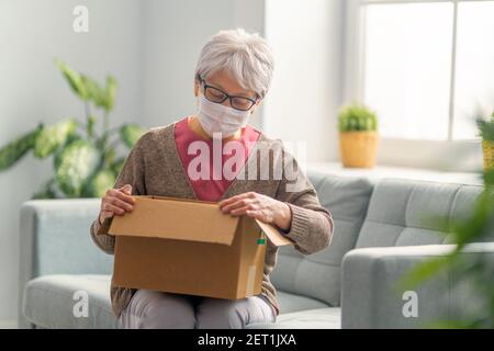 Une femme âgée tient une boîte en carton sur un canapé à la maison. Banque D'Images