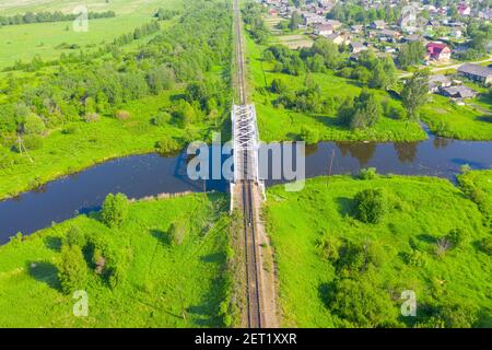 Pont de chemin de fer au milieu de prairies verdoyantes sur une petite rivière dans la campagne, vue aérienne Banque D'Images