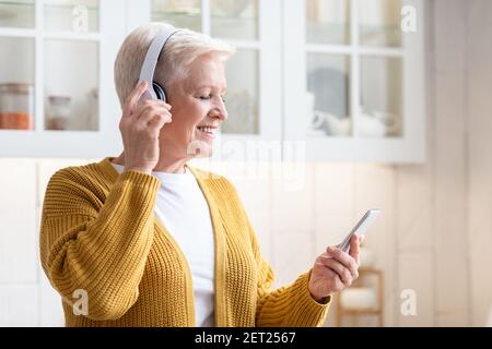 Grand-mère souriante s'amusant, écoutant de la musique sur un smartphone Banque D'Images