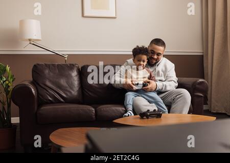 Petit garçon assis sur la hanche de son père et tenant un joystick. Homme aidant un enfant à jouer Banque D'Images