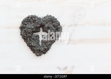 forme d'une croix chrétienne dans un coeur de cendre sur fond de bois blanc avec espace de copie Banque D'Images