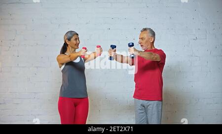couple interracial senior se regardant les uns les autres tout en faisant de l'exercice avec haltères Banque D'Images