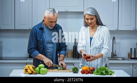 couple interracial âgé préparant une salade fraîche pour le petit déjeuner dans la cuisine Banque D'Images