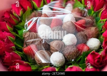 Bouquet cadeau avec roses rouges et fraises fraîches en chocolat noir et flocons de noix de coco. Banque D'Images