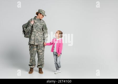 Fille souriante tenant la main de la mère en uniforme militaire arrière-plan gris Banque D'Images