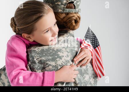 Fille souriante tenant le drapeau américain et embrassant la mère dans l'armée uniforme isolé sur gris Banque D'Images