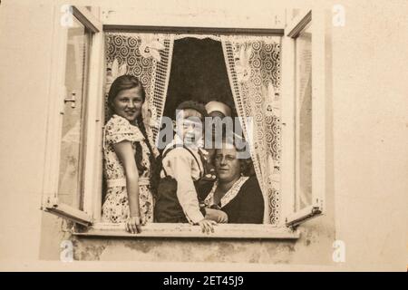 Lettonie - VERS les années 1930 : une famille assise ensemble dans un groupe de seuil de fenêtre tourné. Les enfants vivaient dans un foyer familial de trois générations. Art déco vintage e Banque D'Images