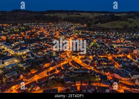 Vue aérienne sur une ville illuminée avec des voitures dans les rues et des lumières orange de lanternes et une colline derrière la petite ville. Banque D'Images