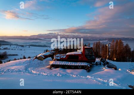 tondeuse à neige recouverte de neige sur fond d'une belle montagne panorama au lever du soleil Banque D'Images