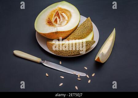 Des tranches de melon juteux mûr frais sur une assiette, un couteau et des graines sur une table noire Banque D'Images