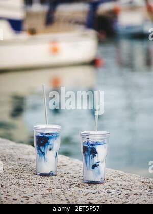 Verre au matcha latte bleu glacé dans des verres écologiques réutilisables avec pailles en verre sur la côte de la Méditerranée en plein air, concentration sélective. Emportez la nourriture pendant le concept de verrouillage Banque D'Images