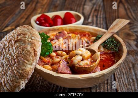 Bol en bois et cuillère avec cuisse de porc fumée et haricots ragoût sur une table rustique Banque D'Images