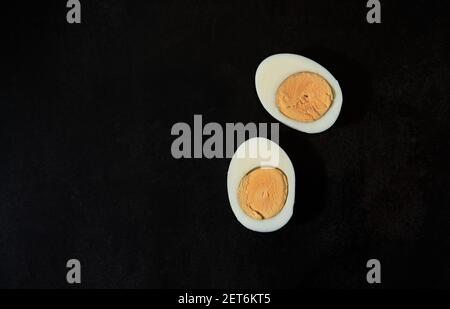 Deux moitiés d'œuf de poulet coupées en deux sur une table de cuisine noire, vue du dessus. Blanc et jaune d'œuf dur. Menu de restaurant minimaliste. Banque D'Images