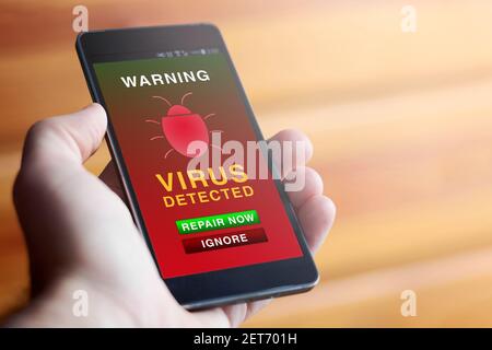 Gros plan de main masculine tenant un téléphone mobile moderne avec un écran d'avertissement antivirus rouge montrant le texte « AVERTISSEMENT : VIRUS DÉTECTÉ ». Concept de sécurité en ligne. Banque D'Images