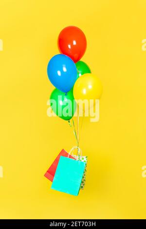 Des sacs en papier et un tas de ballons volent. Vente, présent, concept de livraison. Ballons verts, rouges, jaunes et bleus, et sacs en papier rouges et bleus volant iso Banque D'Images