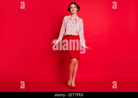 Vue sur toute la longueur de la taille du corps de la jolie fille gaie aux cheveux bruns pose portant de bons vêtements isolés sur fond rouge vif Banque D'Images