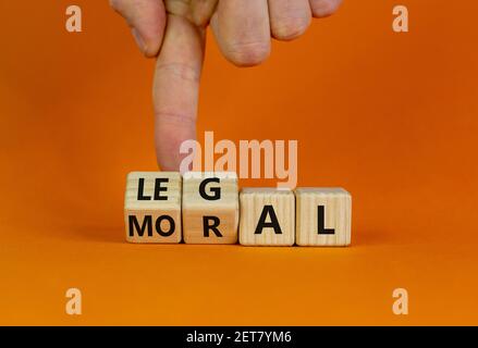 Symbole moral ou légal. La main d'homme d'affaires tourne des cubes en bois et change le mot « oral » en « legal » sur une belle table orange, fond orange. Bus Banque D'Images