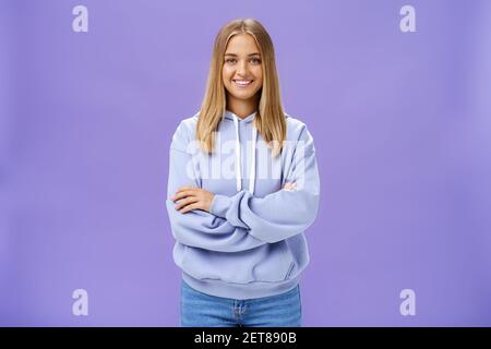 Portrait de charmante femme européenne charismatique avec la peau bronzée dedans un sweat à capuche tendance de grande taille se croisant les mains contre la poitrine en souriant largement appareil photo Banque D'Images