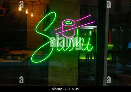Un gros plan d'un panneau lumineux au néon lumineux d'un bar à sushis sur un mur de verre Banque D'Images