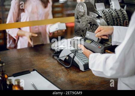 Femme méconnaissable client faisant le paiement dans la pharmacie ancienne, en faisant la bichine de la médecine. Pharmacien homme tenant le terminal, et faisant glisser le crédit du patient Banque D'Images