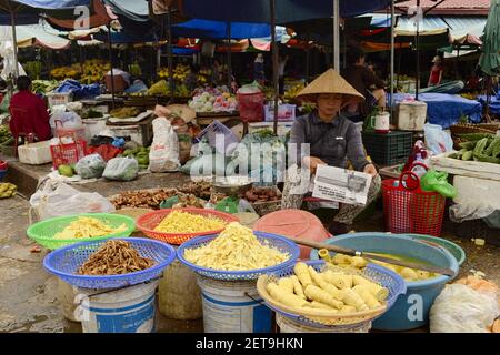 Dong Ha, Vietnam - septembre, 2015: Femme lisant le journal en chapeau vietnamien et vendant des pousses de bambou et d'autres aliments asiatiques sur un marché traditionnel Banque D'Images