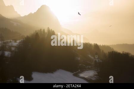 Coucher de soleil épique et lumineux dans les montagnes avec des oiseaux qui s'envollent village de l'église - poussière du sahara Banque D'Images