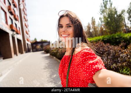 Photo de charmante gaie jeune femme tenir l'appareil photo faire selfie blogger dehors dans le centre-ville à l'extérieur Banque D'Images