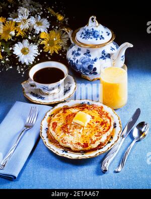 ANNÉES 1970, PLACE DU PETIT DÉJEUNER, VERRE, JUS D'ORANGE, TASSE À CAFÉ SOUCOUPE DE PLATS BLEUS ET BLANCS EMPILEZ DES CRÊPES AVEC DU BEURRE À SIROP PAT - KF14375 PHT001 - SOUCOUPE HARS Banque D'Images