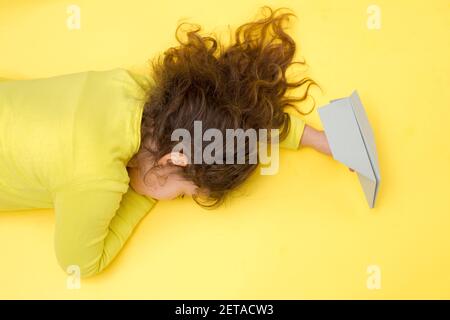 Fille endormi à la main avec un avion en papier gris sur fond jaune. Voyage créatif, concept de vacances pendant Covid-19 dans la couleur tendance 2021 Banque D'Images