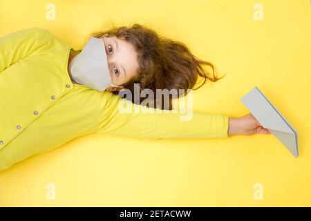 Fille dans un masque de protection gris en main avec un avion en papier gris sur un fond jaune. Voyage créatif, concept de vacances pendant le Covid-19 dans le mode Banque D'Images
