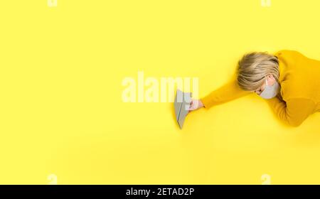 Femme dormant dans masque de protection gris en main avec avion en papier gris sur fond jaune. Concept de voyage Covid-19 créatif dans une couleur tendance Banque D'Images