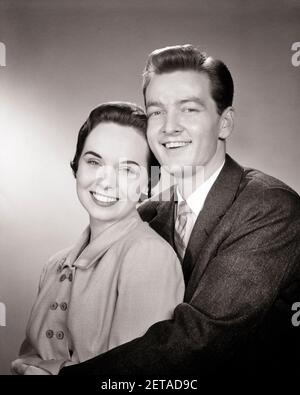 UN COUPLE SOURIANT DES ANNÉES 1950 REGARDANT UN HOMME DE CAMÉRA A DES BRAS AUTOUR FEMME TÊTE SE TOUCHANT - P2617 HAR001 HARS FORTE JOIE HEUREUSE SATISFACTION DE STYLE DE VIE FEMMES TÊTES MARIÉES STUDIO SHOT CONJOINT ÉPOUX MAISON VIE COPIE ESPACE AMITIÉ DEMI-LONGUEUR HUG DAMES PERSONNES S'OCCUPANT DES HOMMES CONFIANCE EMBRASSANT LES EXPRESSIONS B&W PARTENAIRE CONTACT VISUEL COMBINAISON BRUNETTE ET CRAVATE BONHEUR JOYEUX FIERTÉ SOURIRES HAUTE TECHNOLOGIE JOYEUX STYLE PERSONNEL ATTACHEMENT AFFECTION COOPÉRATION ÉMOTION TOGETHERNESS FEMMES JEUNE ADULTE HOMME NOIR ET L'ETHNIE BLANCHE CAUCASIENNE HAR001 ANCIEN MODE Banque D'Images