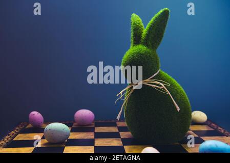 Concept de Pâques créatif et tendance. Jeu d'échecs de Pâques avec des œufs de couleur et lapin vert de Pâques sur fond bleu foncé. Mise au point sélective Banque D'Images