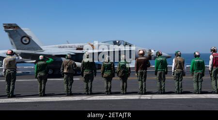 Les équipages de plate-forme de la Marine américaine sont à l'attention d'un avion de chasse F/A-18C Hornet avec les chasseurs de la mort de l'escadron d'attaque de chasseurs marins 323 qui se lance à partir du pont de vol à bord du porte-avions de la classe Nimitz USS Nimitz le 25 février 2021 dans l'océan Pacifique. Banque D'Images