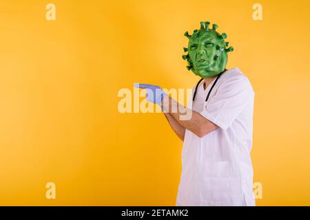 Médecin - infirmière en coronavirus déguisée portant un masque en latex - virus Covid-19 pointant de côté sur fond jaune. Concept de coronavirus Banque D'Images