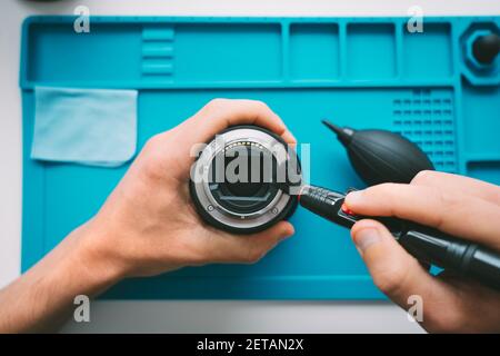 Homme nettoyant la lentille de son appareil photo avec une brosse pour objectif ou un stylo nettoyant pour objectif et un souffleur d'air. Entretien de l'équipement de photographie Banque D'Images