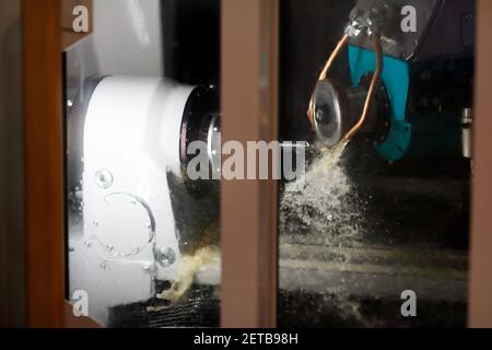 Processus de broyage avec du liquide de refroidissement. Vue par la porte vitrée de la machine à meuler. Mise au point sélective. Banque D'Images