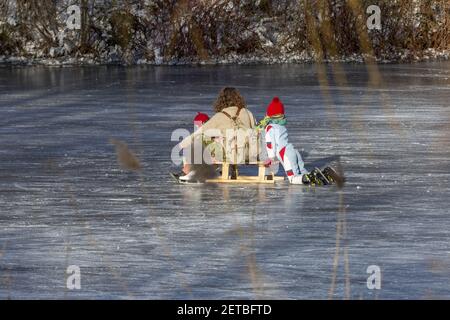 ZUTPHEN, PAYS-BAS - 13 févr. 2021: Mère et enfants sur un traîneau profitant de l'hiver gelée rivière Berkel vue à travers le roseau au coucher du soleil Banque D'Images