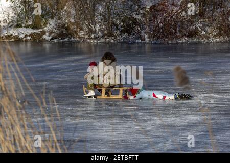 ZUTPHEN, PAYS-BAS - 13 févr. 2021: Traîneau avec mère sur patins assis avec un enfant et un autre à plat sur la glace en profitant de l'hiver gelé Banque D'Images