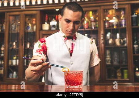 Barman préparant un cocktail negroni au pamplemousse. Il met de l'essence de la peau de pamplemousse dans le verre à cocktail sur le comptoir Banque D'Images