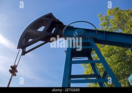 Bloc de pompage industriel avec corps encadré peint en bleu et élément de bascule noir avec corde flexible sur l'arrière-plan de ciel bleu nuageux et frénésie Banque D'Images