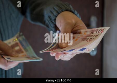 Une femme en tricot gris tient trois billets de dix euros avec sa main gauche contre la porte avant marron. Concept: Paiement avec l'installateur, plombier Banque D'Images