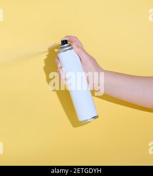 main tenant une boîte et vaporisant un produit sur un fond jaune. maquette pour la conception du produit. hygiène ou insecticide. nettoyage et entretien ménager Banque D'Images